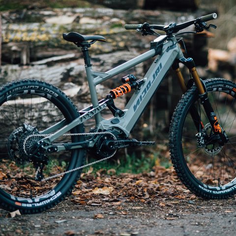 Hotel mit Fahrradverleih in Bayern gesucht? Graues Mountainbike mit vollem Federweg vor Holzhaufen im Wald