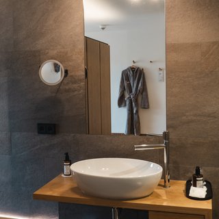 Inklusivleistungen: Alles, was die Hirschen begehren. Modernes Badezimmer mit Waschbecken, Spiegel und grauem Bademantel an der Wand