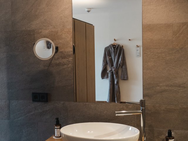 Romantik Hotel Hirschen: Bildergalerie Modernes Badezimmer mit Waschbecken, Spiegel und grauem Bademantel an der Wand
