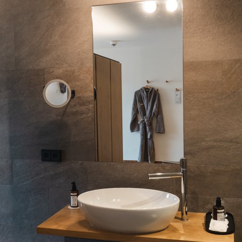 Romantik Hotel Hirschen: Gastgeber & Werte Modernes Badezimmer mit Waschbecken, Spiegel und grauem Bademantel an der Wand