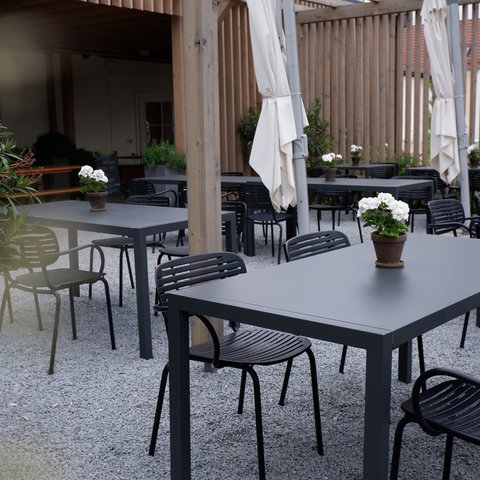 Beer garden in Parsberg: HirschenBlobb Empty outdoor seating with black chairs and pots with white flowers