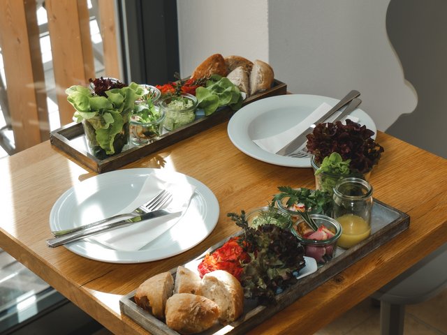 Romantik Hotel Hirschen: Bildergalerie Zwei eingedeckte Teller mit frischem Brot, Salat und kleinen Gläsern auf Holztisch