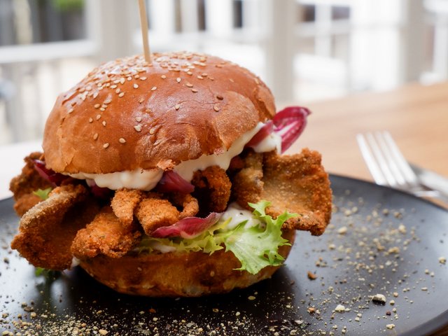 Romantik Hotel Hirschen: Bildergalerie Panierter Fleischburger mit Salat und Soße auf einem schwarzen Teller