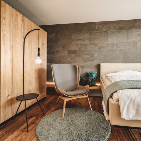 Romantik Hotel Hirschen: Gastgeber & Werte Modern eingerichtetes Schlafzimmer mit grauem Stuhl und Holzschrank