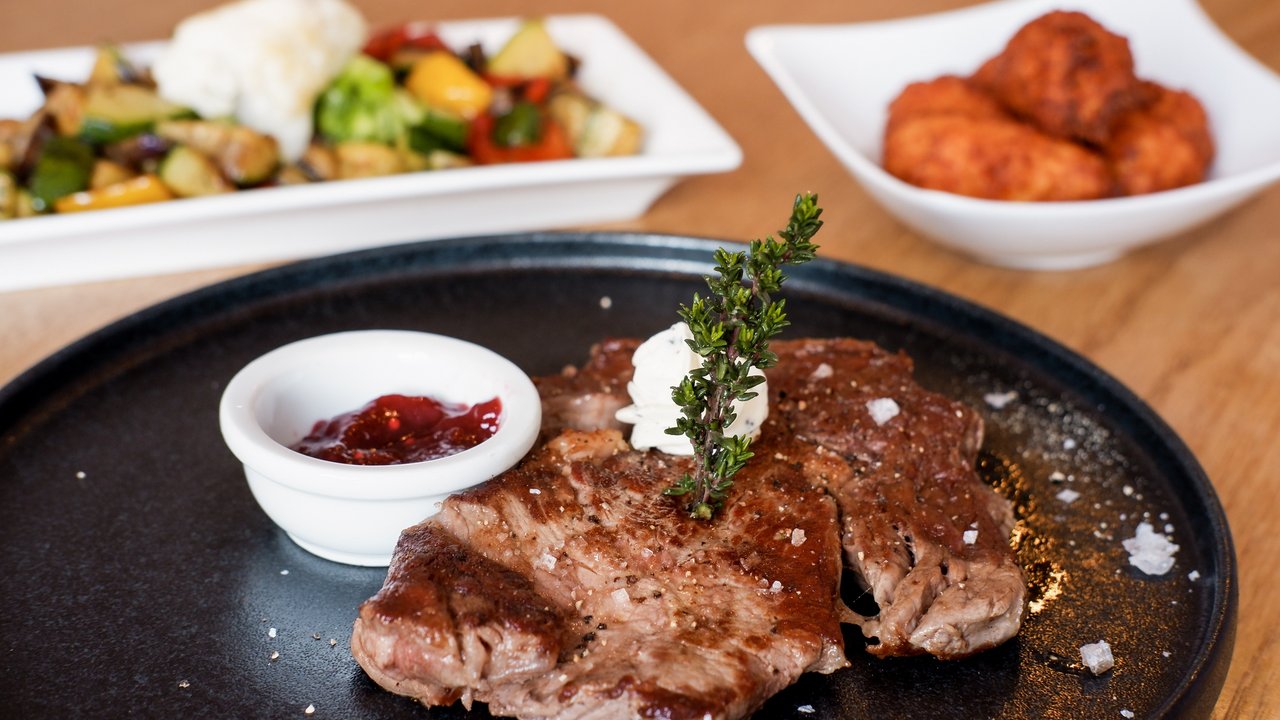 Gegrilltes Steak mit Kräuterbutter, Sauce und Gemüse auf Tellern