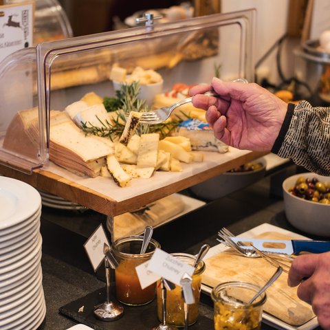 Brunch - das Langschläferfrühstück Person nimmt Käse mit Gabel von Käseplatte im Buffet