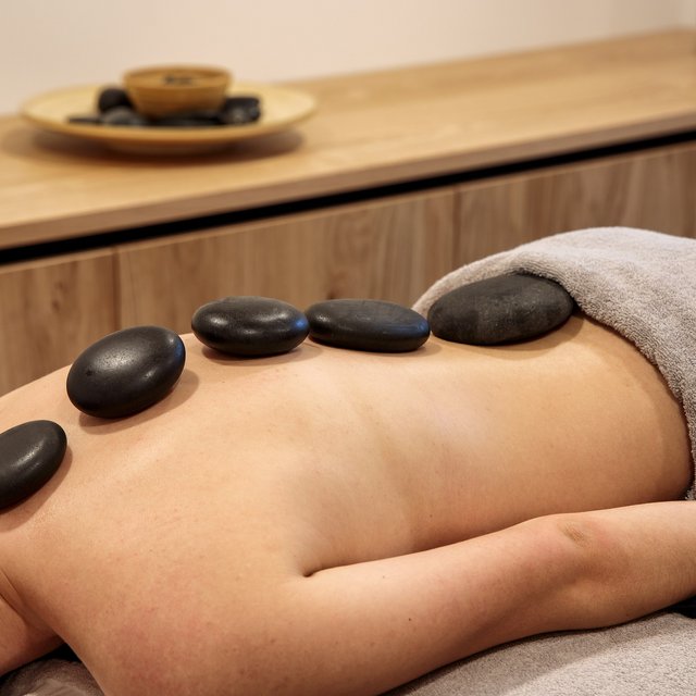 Wellnesshotel in der Oberpfalz: schwitzen & schwimmen Person bei Hot-Stone-Massage mit schwarzen Steinen auf dem Rücken