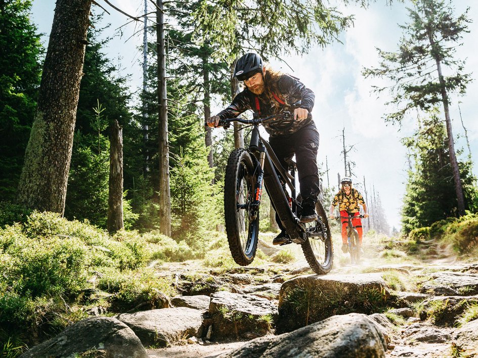 Hiking in Upper Palatinate: Active in nature Mountain bikers jumping over rocky forest trail on a sunny day