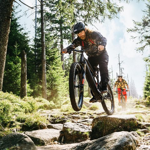 Looking for a hotel with bike rental in Bavaria? Mountain bikers jumping over rocky forest trail on a sunny day