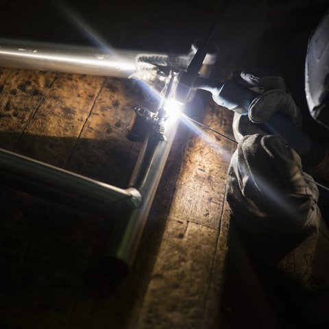 Hotel mit Fahrradverleih in Bayern gesucht? Handschuhtragender Schweißer verbindet Metallrahmen mit Schutzhelm