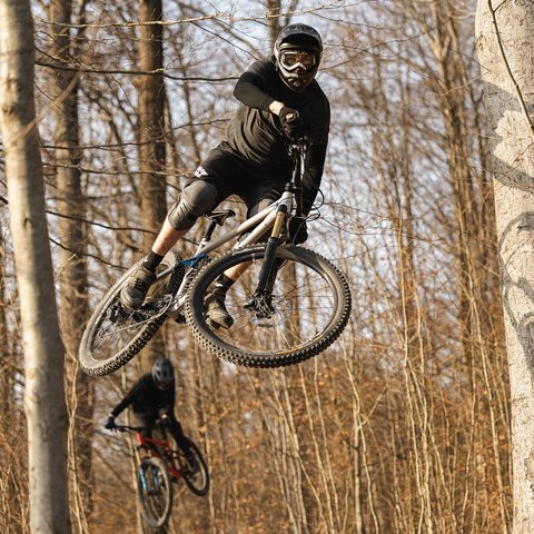 Hotel mit Fahrradverleih in Bayern gesucht? Mountainbiker springt mit Helm und Schutzkleidung durch herbstlichen Wald
