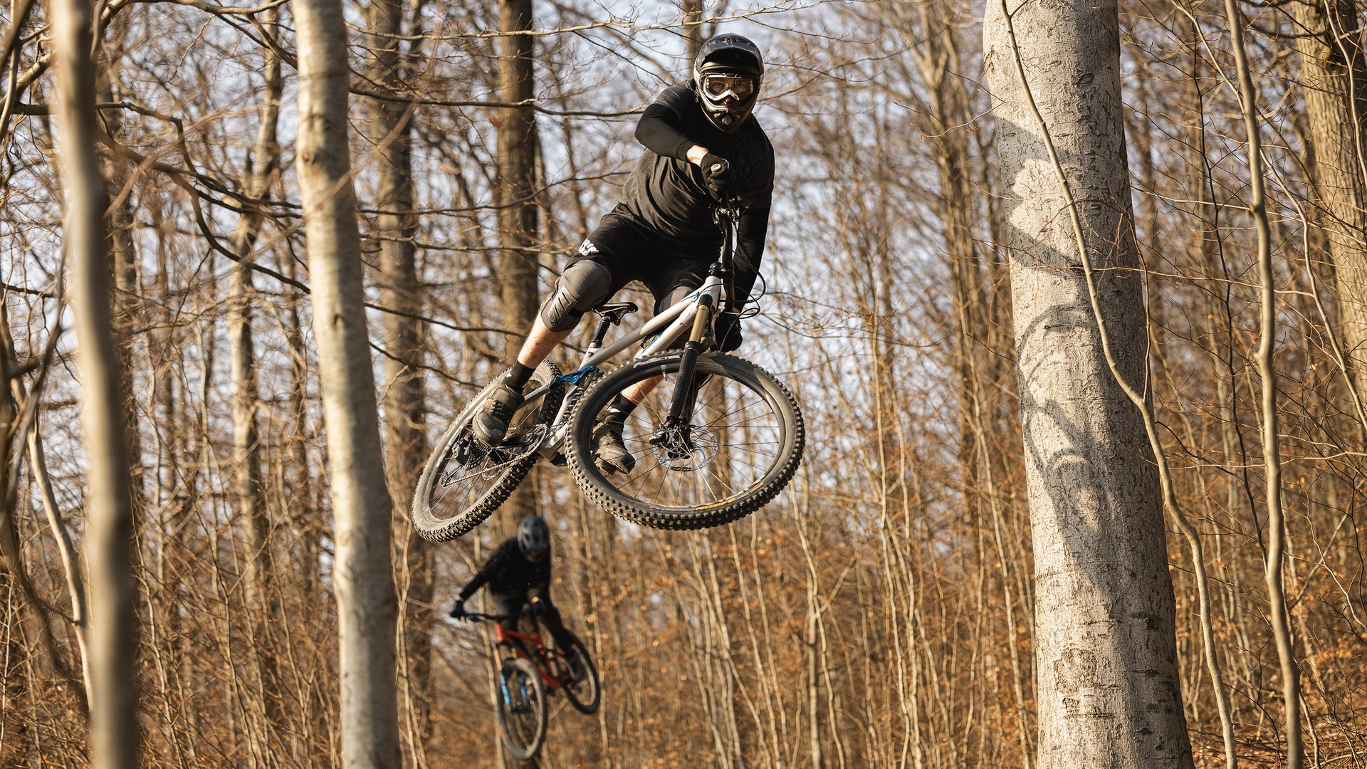 Looking for a hotel with bike rental in Bavaria? Mountain biker jumping with helmet and pads in autumn forest