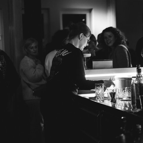 Hirschenblobb: Our bar Bartender working behind the bar in a dimly lit bar with customers in the background