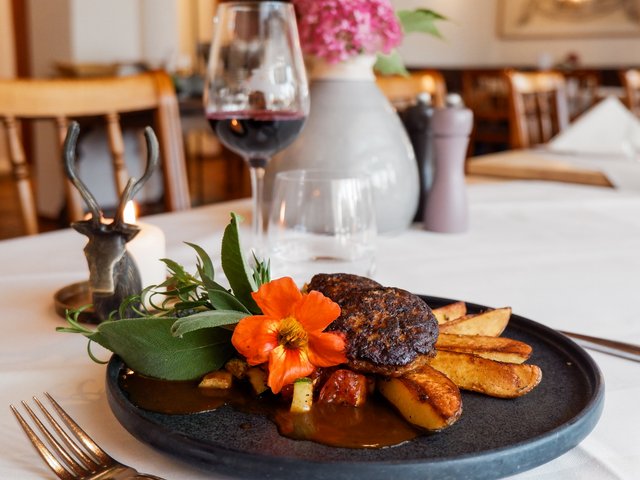 Romantik Hotel Hirschen: Bildergalerie Gehobenes Gericht mit Fleisch, Kartoffelspalten, Kräutern und Blume in elegantem Restaurant