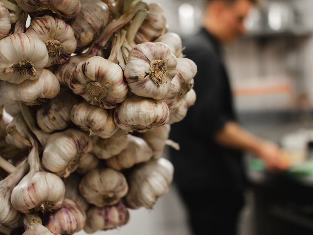 Romantik Hotel Hirschen: Bildergalerie Bündel Knoblauchknollen im Vordergrund in einer Küche mit unscharfer Person