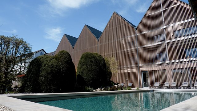 Ferienwohnung in der Oberpfalz gesucht? Moderner Holzbauten-Komplex mit Schwimmbad und gepflegtem Garten unter blauem Himmel