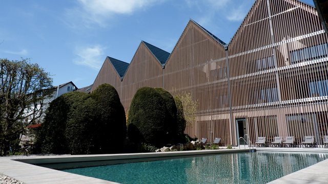 Ferienwohnung in der Oberpfalz gesucht? Moderner Holzbauten-Komplex mit Schwimmbad und gepflegtem Garten unter blauem Himmel