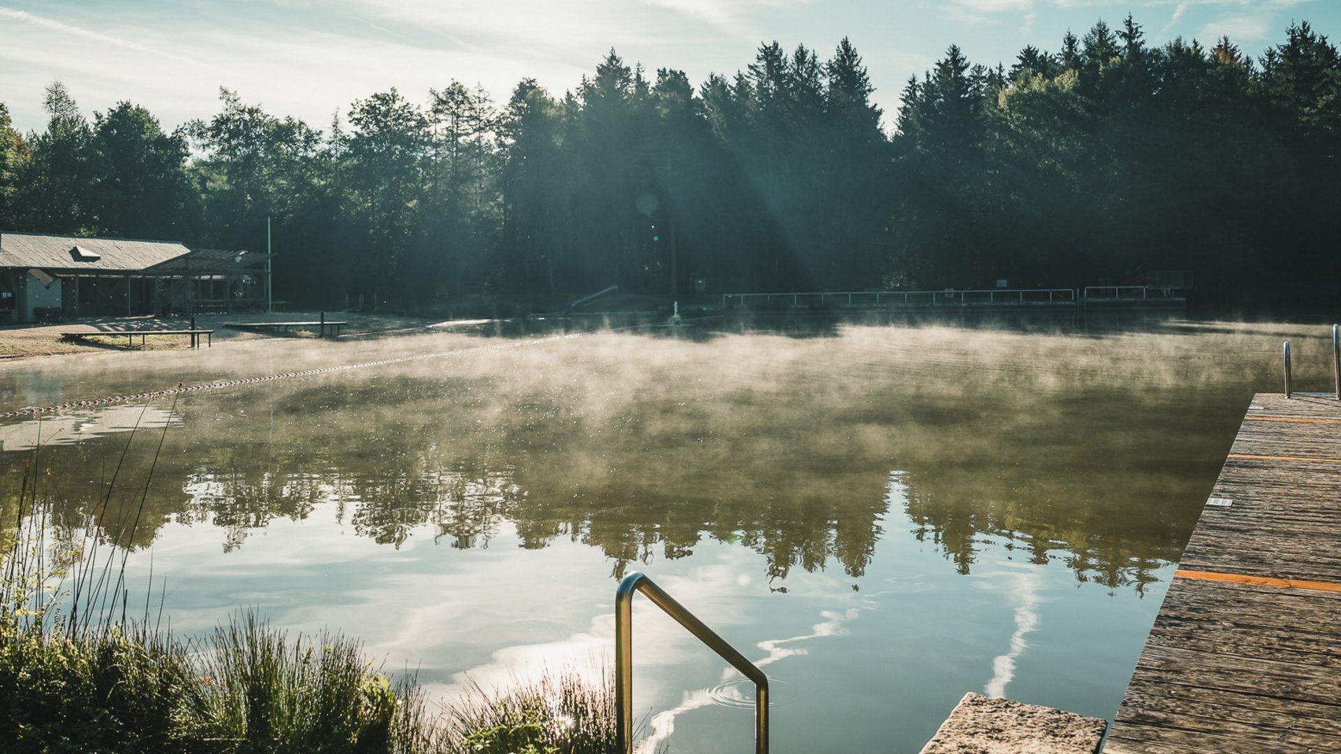 Badeseen Morgennebel über einem See mit Holzsteg und Wald im Hintergrund