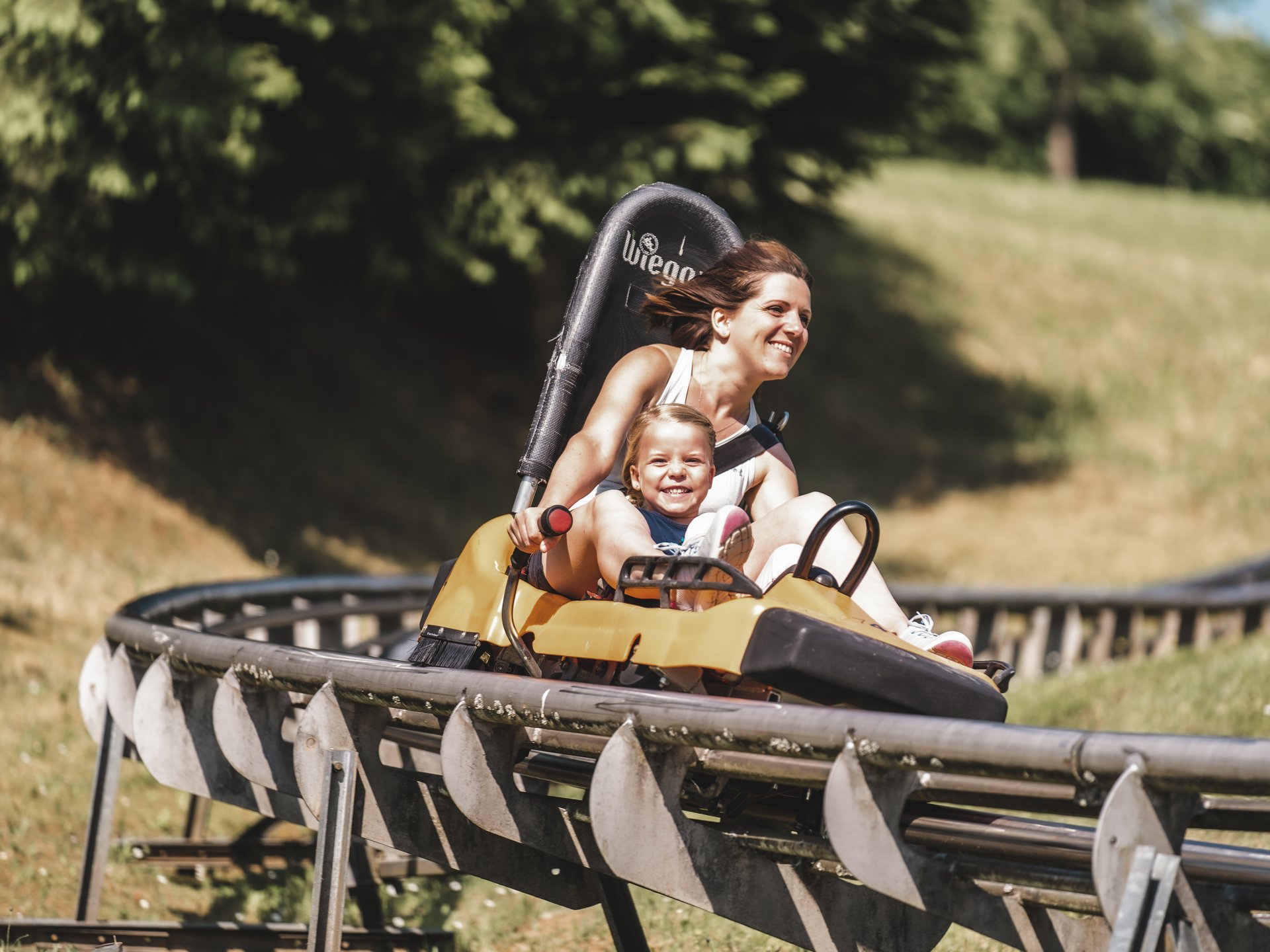 Wandern, Radfahren & Natur erleben Mutter und Kind fahren fröhlich auf einer Sommerrodelbahn im Freien
