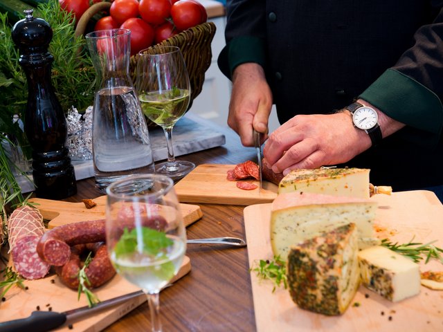 Romantik Hotel Hirschen: picture gallery Person slicing salami near assorted cheeses and drinks on wooden boards
