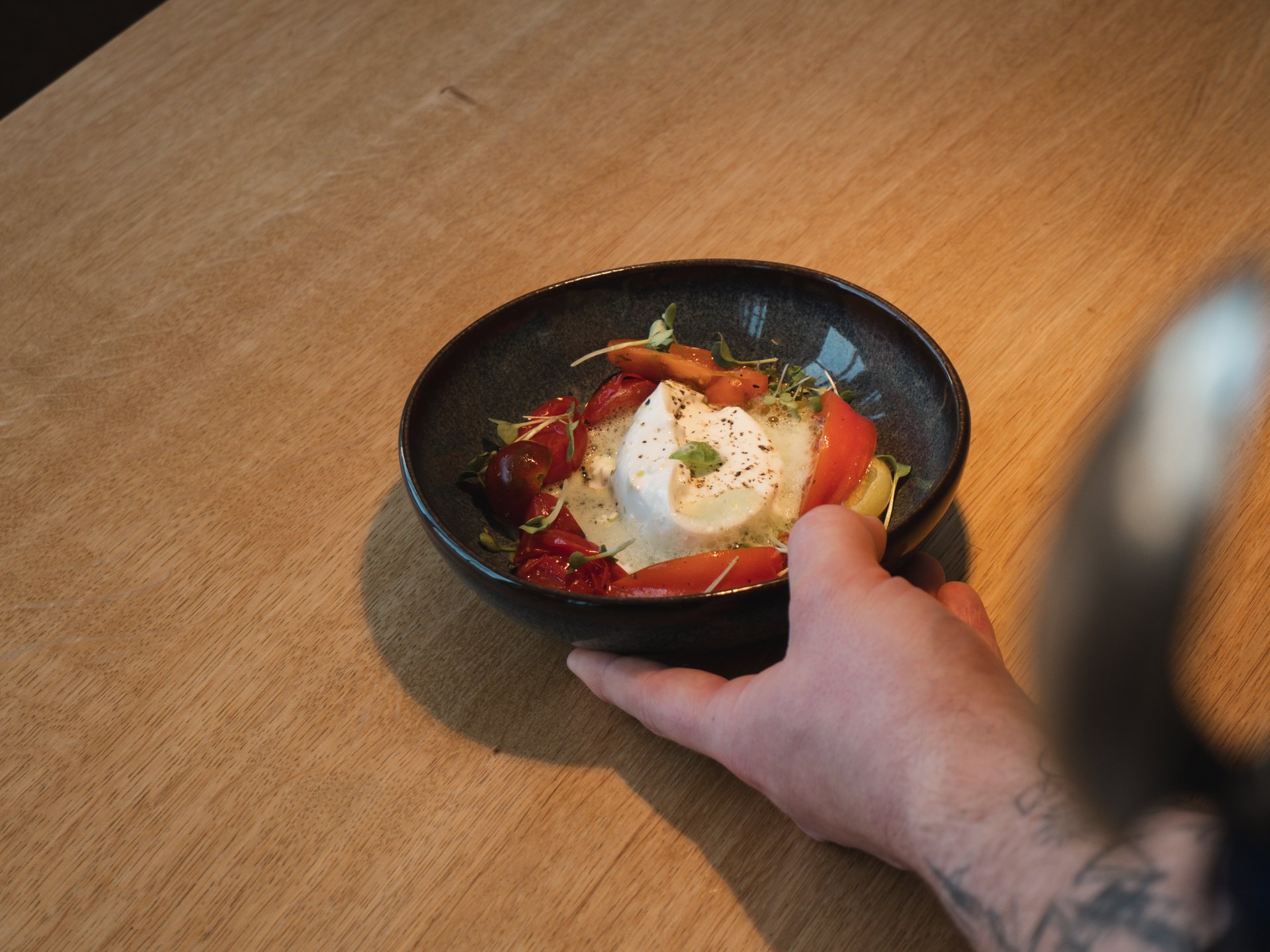 Events & Culinary Experiences in Parsberg Hand holding a bowl with burrata cheese and tomatoes on a wooden table