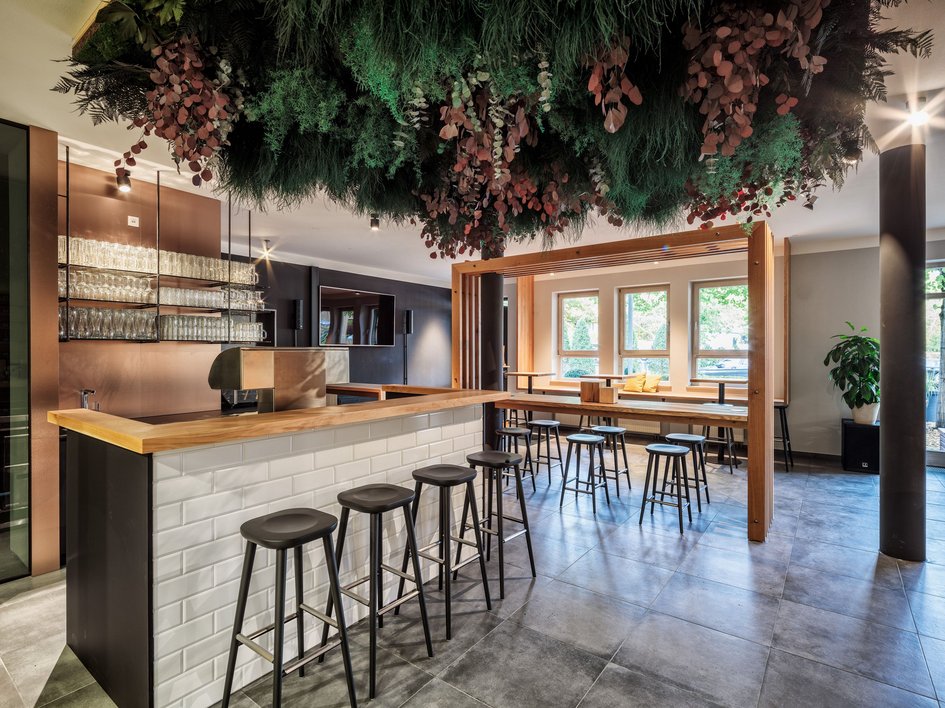 Hotel mit frühem Check-in Moderner Barbereich mit Hockern, Holztresen und hängender Pflanzeninstallation