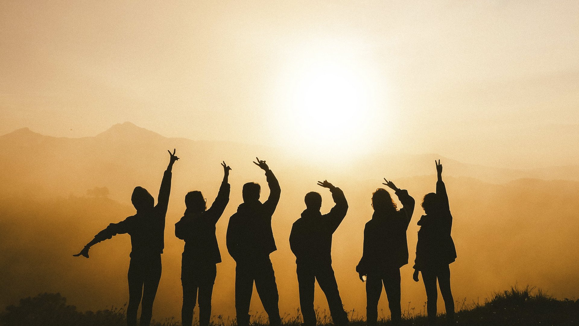 Mental Leadership Retreat Schatten von sechs Personen mit erhobenen Armen vor der Sonne und Bergen