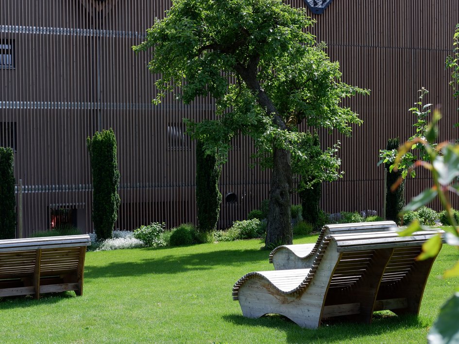 Entspannung in der Oberpfalz: Garten & Ruheräume Holzliegen im Park vor modernem Gebäude und Bäumen auf grünem Rasen