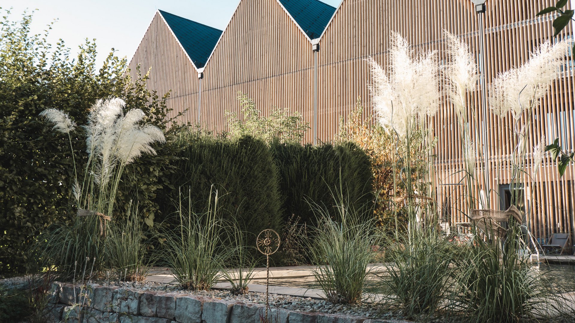 Wellness Oberpfalz – GartenSPA im Romantik Hotel Hirschen Modern building with zigzag rooflines behind a garden of ornamental grasses