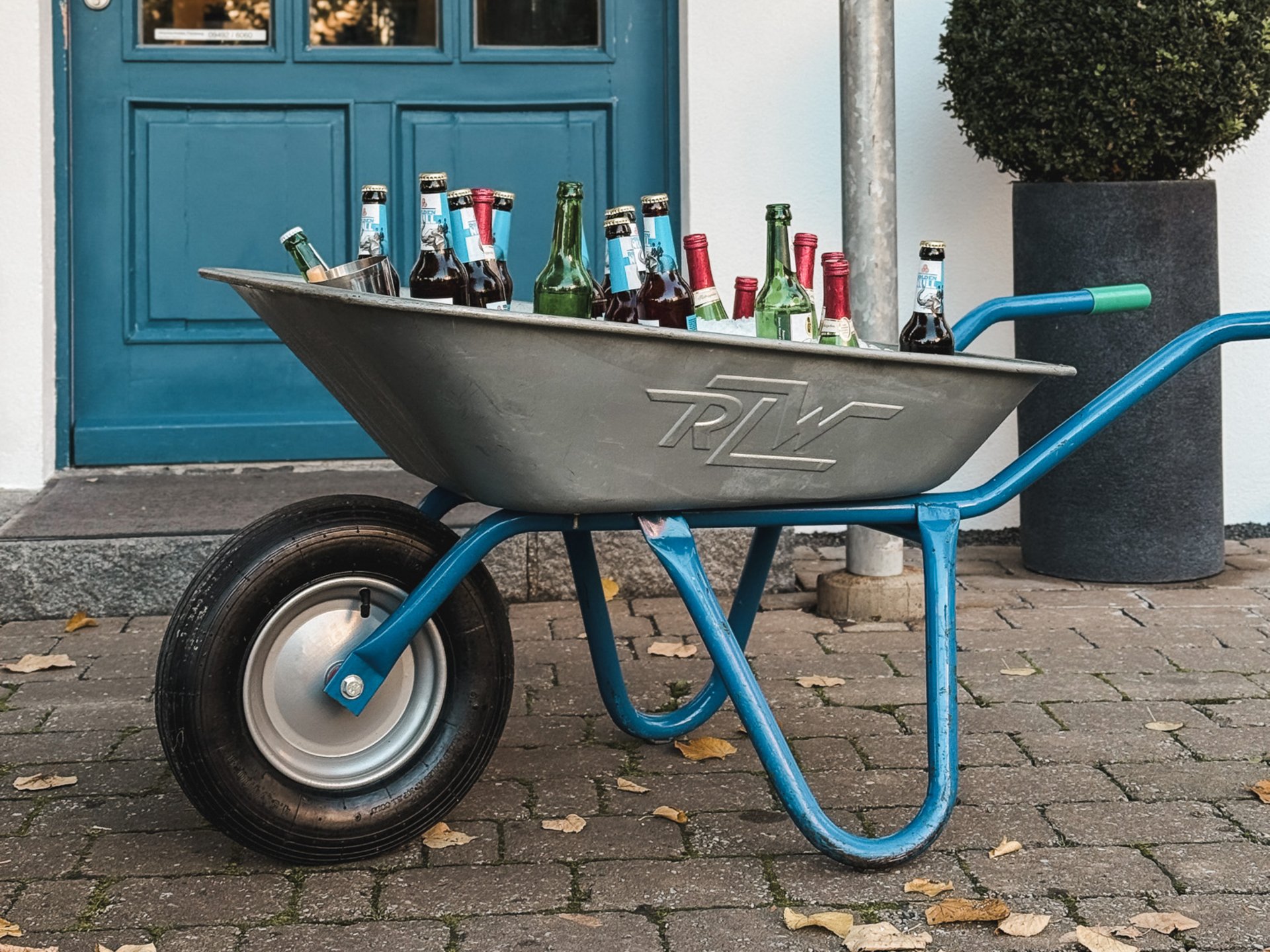 Teambuilding, Firmenevents & Rahmenprogramme Schubkarre mit Bierflaschen vor blauem Eingang und Schild der Hirschen Blobb Bar