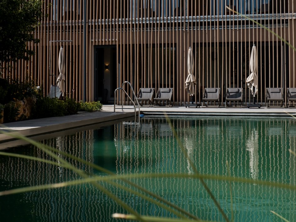 Nachhaltige Hotels in Deutschland gesucht? Schwimmbad mit Liegestühlen vor modernem Holzgebäude bei Tageslicht