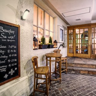 Angebote aus dem Romantik Hotel Hirschen Eingang eines Restaurants mit geöffneten Holzstühlen und Tischen und einer Öffnungszeiten-Tafel