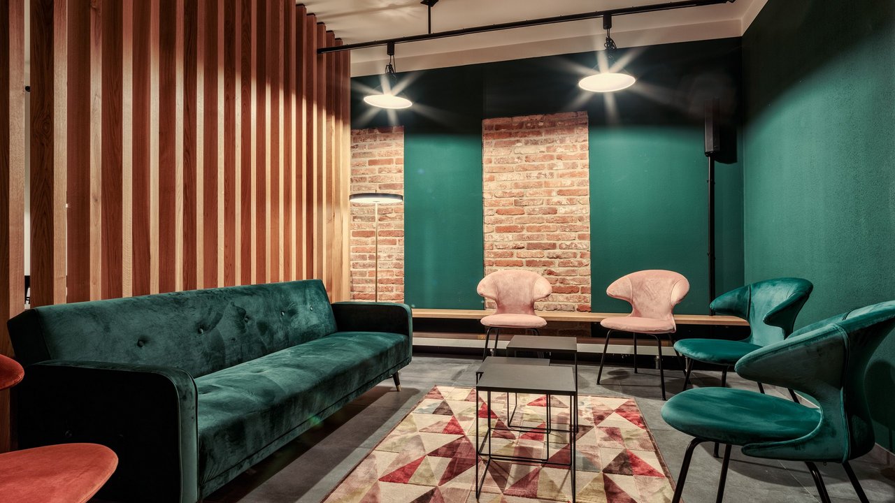 Modernes Wohnzimmer mit grünem Sofa, buntem Teppich und rosa Stühlen