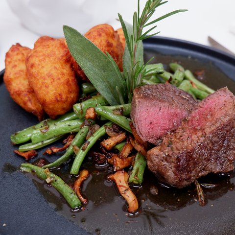 Kulinarik & Genuss in der Oberpfalz Gegrilltes Steak mit grünen Bohnen, Pilzen und Kartoffelpuffern auf schwarzem Teller