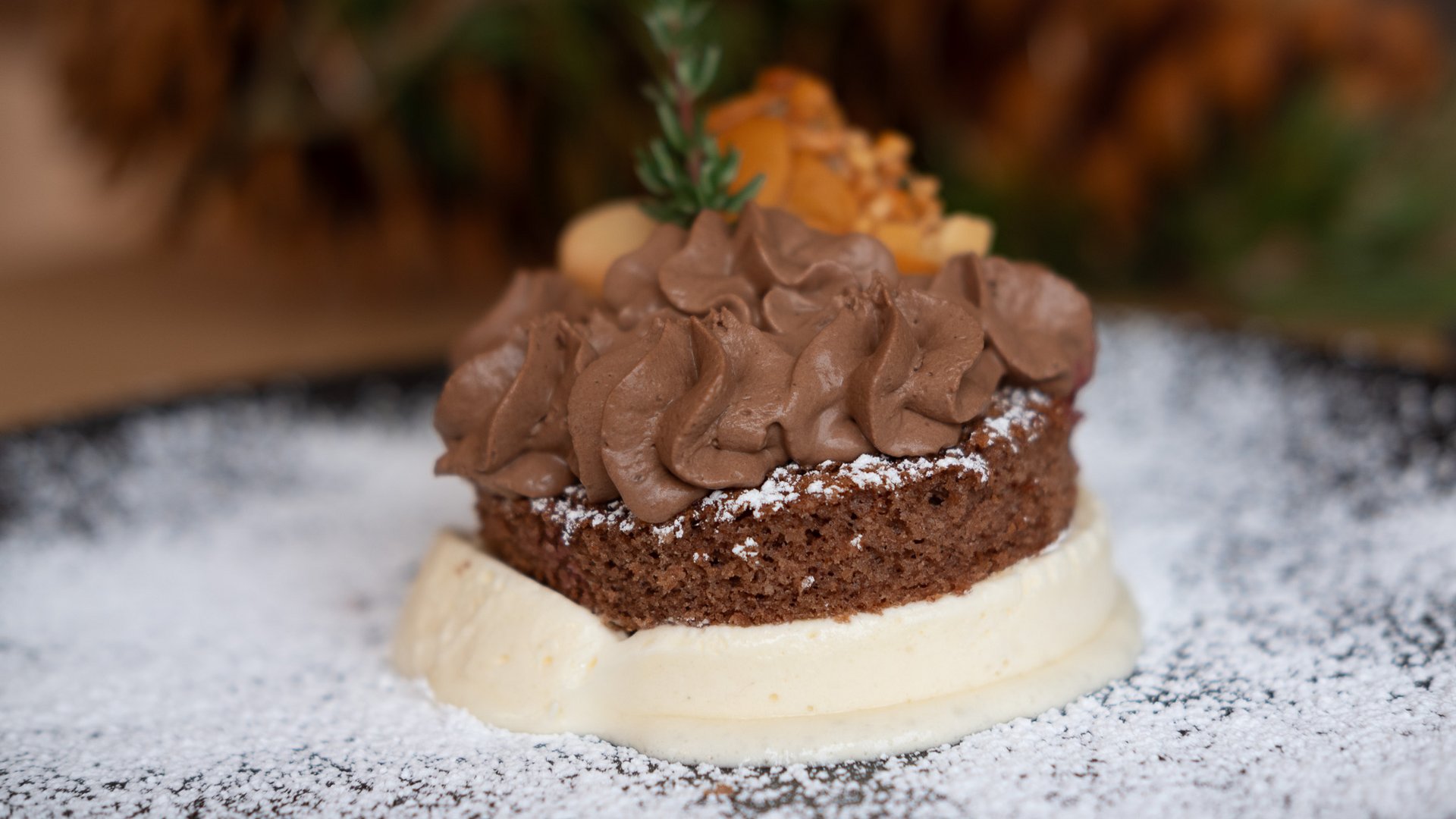 Weihnachtsmenüs 2025 Kleiner Schokoladenkuchen mit Creme und Puderzucker auf schwarzem Teller