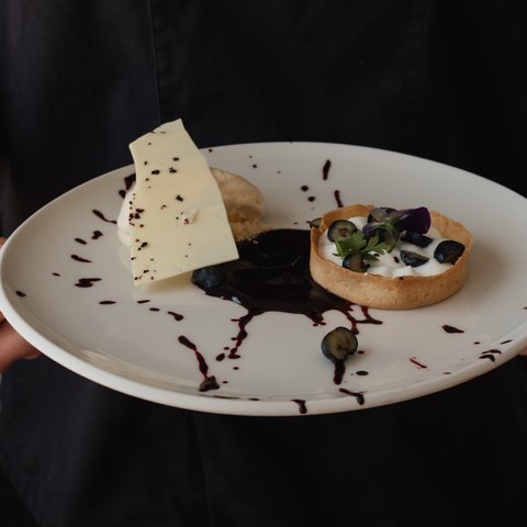 Romantik Hotel Hirschen: Gastgeber & Werte Hand hält Teller mit Desserttarte, Beeren, weißer Schokolade und Soße