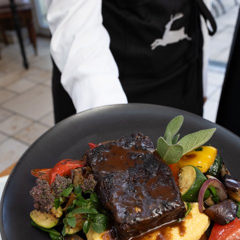 Gasthof & Restaurant in Parsberg mit regionaler Küche Geschmortes Fleisch mit Sauce, Polenta und Gemüse auf einem Teller, serviert von einer Person