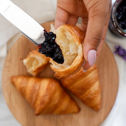 Eco-friendly hotel in Germany with Hirschenmanufaktur Hand holding croissant piece being spread with dark jam
