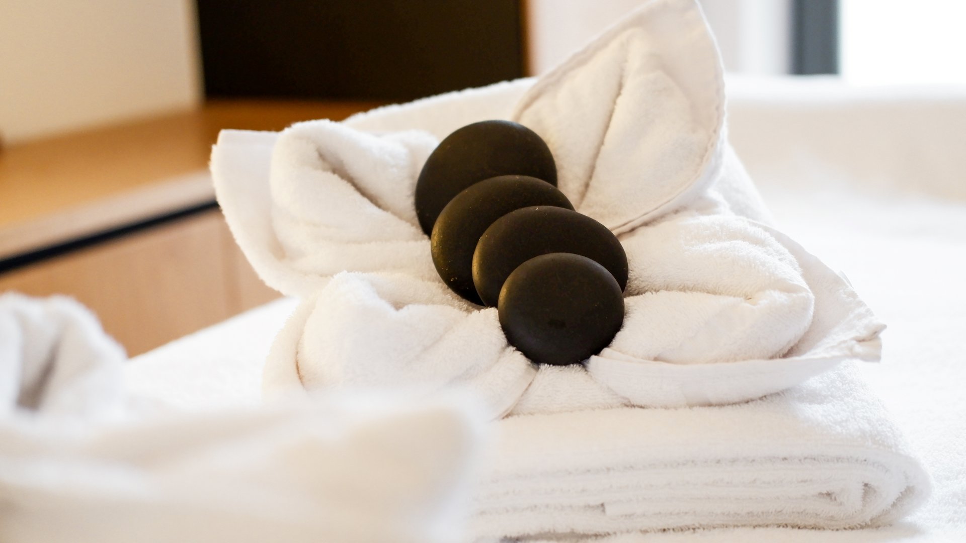Wellness in der Oberpfalz: Massage & Beauty Schwarze Massagesteine auf zusammengerolltem weißen Handtuch