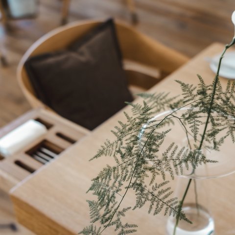 Restaurant in Parsberg: Gourmet genießen Weiße Blume und Farn in Glasvase auf Holztisch neben Stuhl mit braunem Kissen