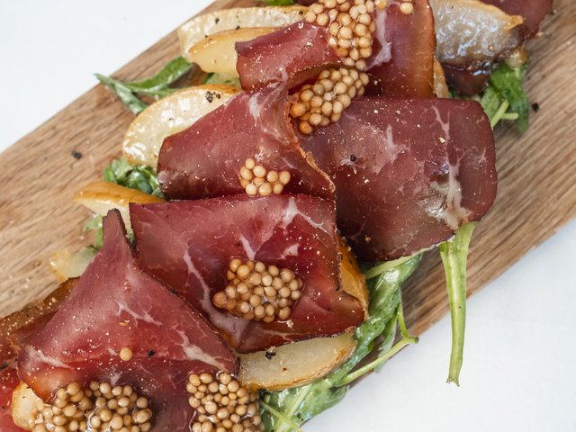 Gasthof & Restaurant in Parsberg mit regionaler Küche Dünne Scheiben gepökeltes Fleisch mit Senfkörnern, Salatgrün und Birne auf einem Holzbrett
