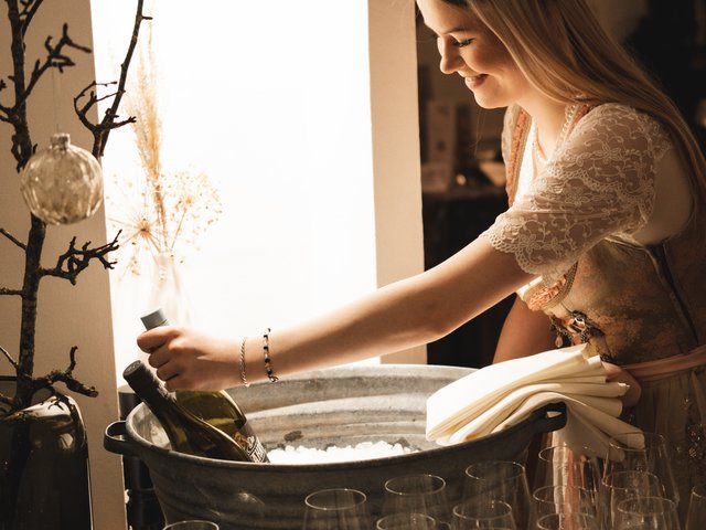 Romantik Hotel Hirschen: Bildergalerie Frau holt Weinflasche aus Eisbehälter, viele leere Weingläser davor