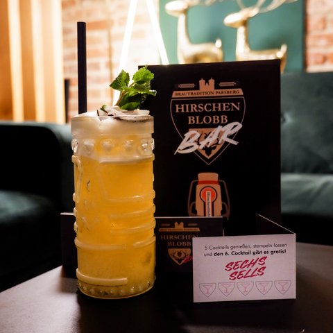 Hirschenblobb: unsere Bar Cocktailglas mit Getränk und Minzblatt vor Bar-Menükarte und Werbeblatt