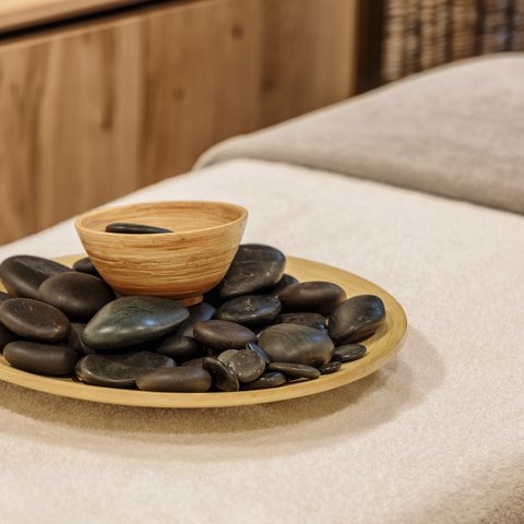 Day wellness in Upper Palatinate Black massage stones in wooden bowl on massage table with towels