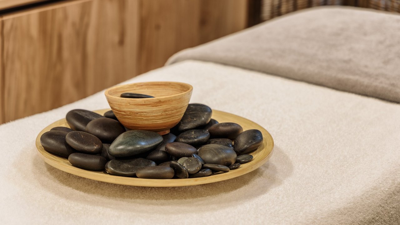 Schwarze Massage-Steine auf Holzschale auf Massagetisch mit Handtüchern