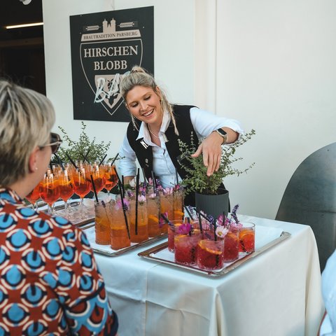 Kulinarik & Genuss in der Oberpfalz Frau serviert bunte Cocktails mit Kräutern auf einem gedeckten Tisch