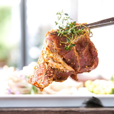 Beer garden in Parsberg: HirschenBlobb Seasoned steak piece with fresh herbs held by tweezers