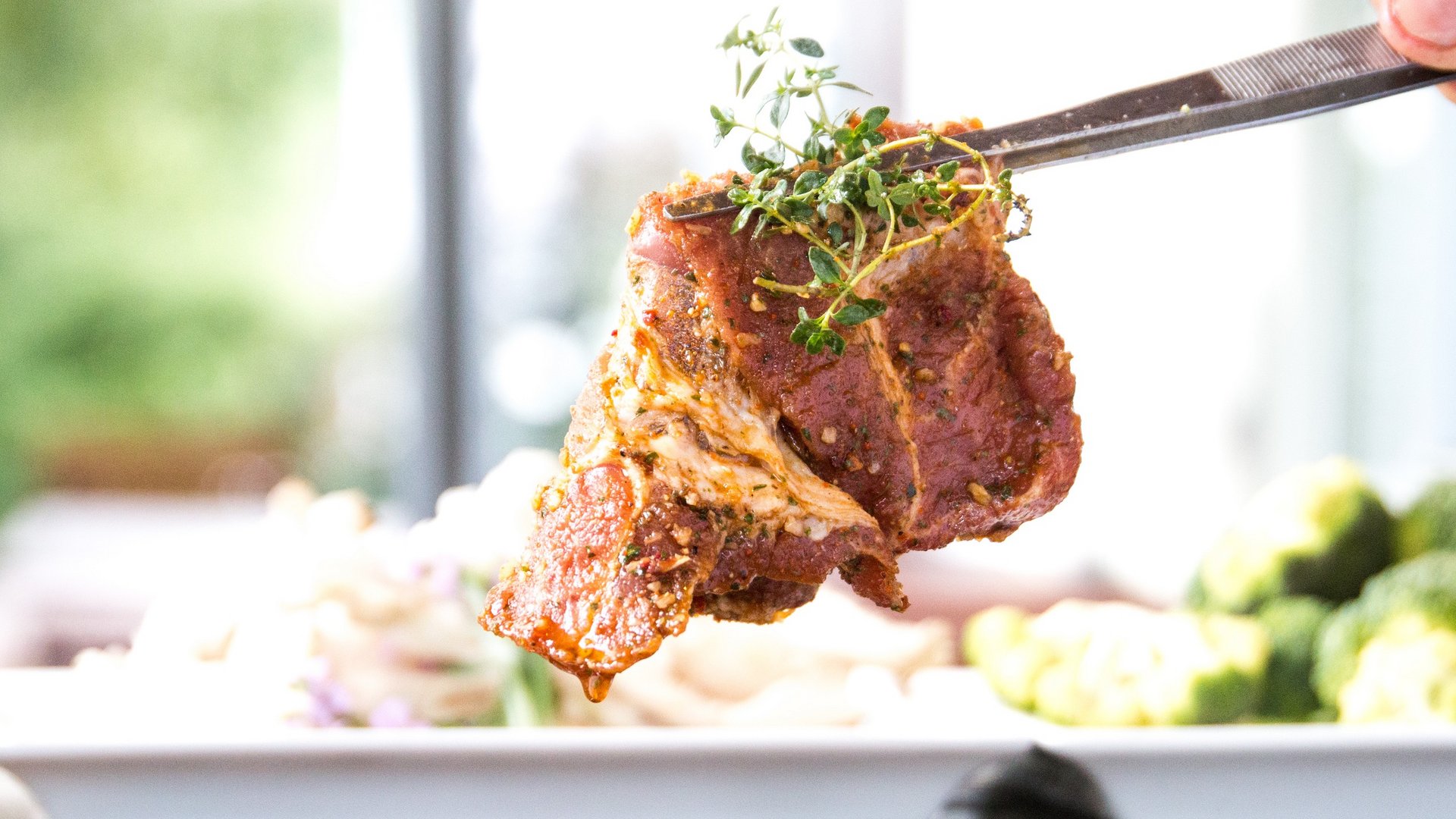 Beer garden in Parsberg: HirschenBlobb Seasoned steak piece with fresh herbs held by tweezers