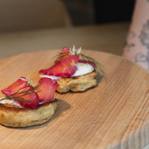 Romantik Hotel Hirschen: Gastgeber & Werte Zwei Canapés mit Lachs und Kräutern auf einem Holzbrett