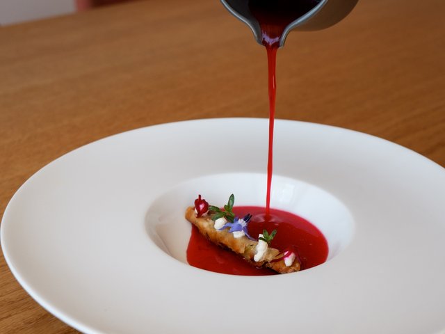 Romantik Hotel Hirschen: Bildergalerie Rote Sauce wird über ein dekoriertes Gericht in einer weißen Schale gegossen